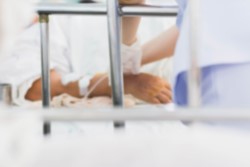 Bildet viser en pasients hånd som blir behandlet av helsepersonell, mens pasienten ligger i en seng.