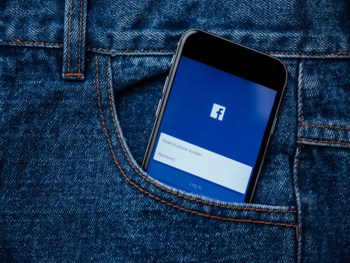 En smarttelefon med facebook sin logo på skjermen stikker opp av en bukselomme